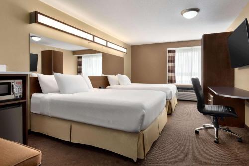 a hotel room with two beds and a desk at Microtel Inn & Suites by Wyndham Estevan in Estevan