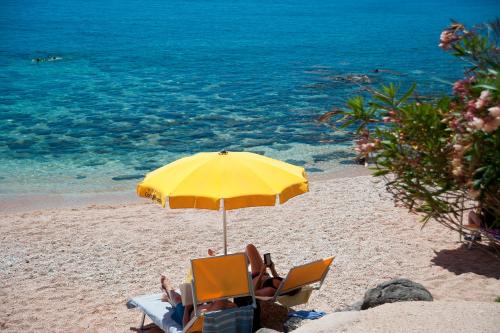 two people sitting in chairs under an umbrella on a beach at Costa Dorada in Cala Gonone