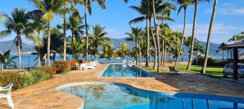 a resort swimming pool with palm trees and the water at Pousada Casa Amarela in Ilhabela