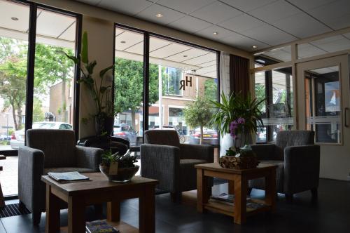 a waiting room with chairs and tables and windows at Hotel Rozenburg in Rozenburg