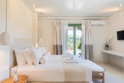 a white bedroom with a large bed and a window at Casa Di Fiori Andros Suites in Andros