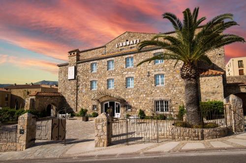 a building with a palm tree in front of it at Hôtel L'Abbaye in Calvi