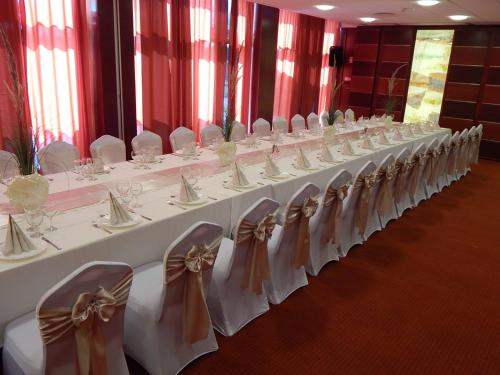 a row of tables with white chairs with bows at Csipke Hotel in Kiskunhalas