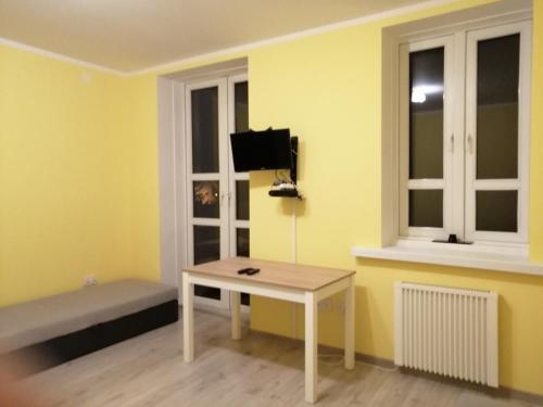 Habitación con mesa y TV en una pared amarilla. en Apartament Stanisławskiego, en Łowicz