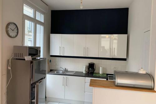 une cuisine avec des placards blancs et une horloge murale dans l'établissement Le Balcon de Notre Dame Le Treport - Locations ISAHORA, au Tréport