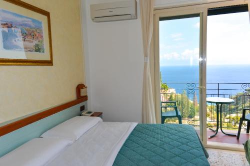 a bedroom with a bed and a balcony with the ocean at Hotel Condor in Taormina