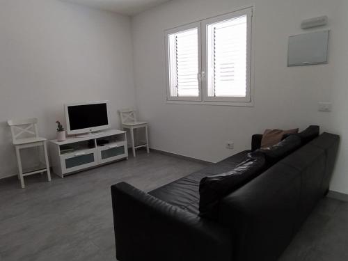 ein Wohnzimmer mit einem schwarzen Sofa und einem TV in der Unterkunft Casa Blanca La Restinga in La Restinga
