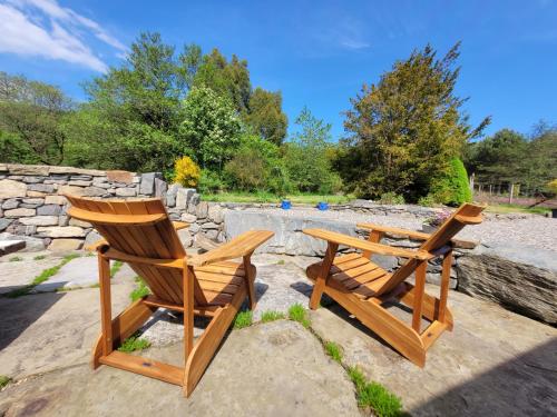 two wooden chairs sitting next to a stone wall at Loch Lomond Blair Byre in Rowardennan