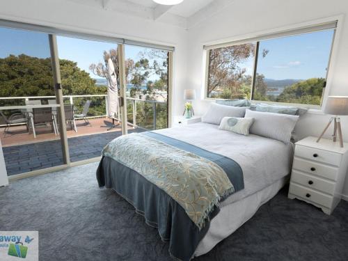 a bedroom with a large bed and large windows at Eight Lakes in Merimbula