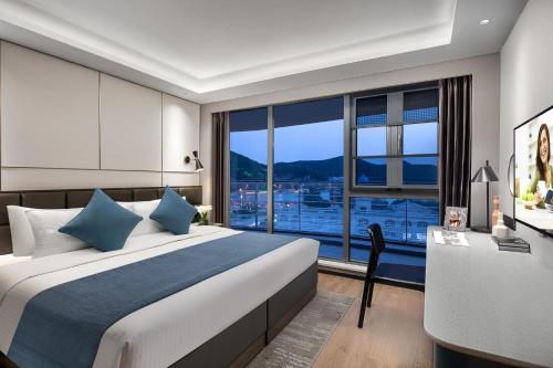 a bedroom with a bed and a desk and a large window at Citadines Yunlong Lake Xuzhou in Xuzhou