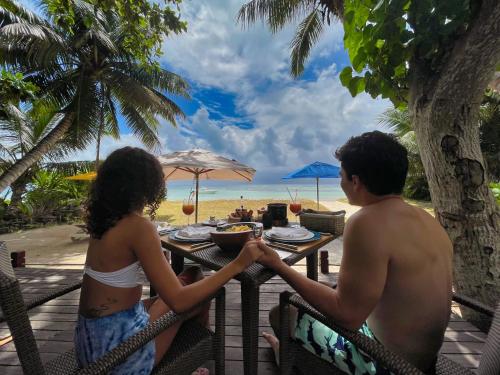 a man and a woman sitting at a table on the beach at Dhevatara Beach Hotel in Grand'Anse Praslin