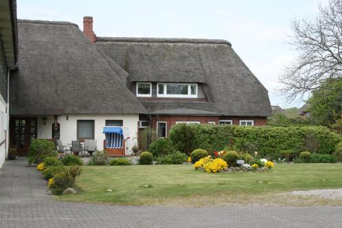 a house with a thatched roof and a yard with flowers at Ferienwohnungen im Hotel garni zur Post in Utersum