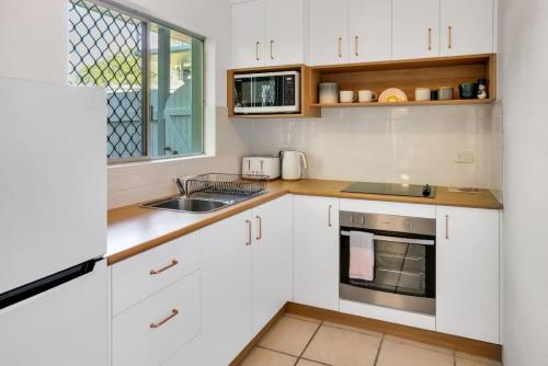 eine Küche mit weißen Schränken und einer Spüle und einem Fenster in der Unterkunft Tropicana Hideaway in Cairns North