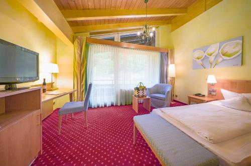 a bedroom with a bed and a television and a chair at Ringhotel Mönch`s Waldhotel in Unterreichenbach