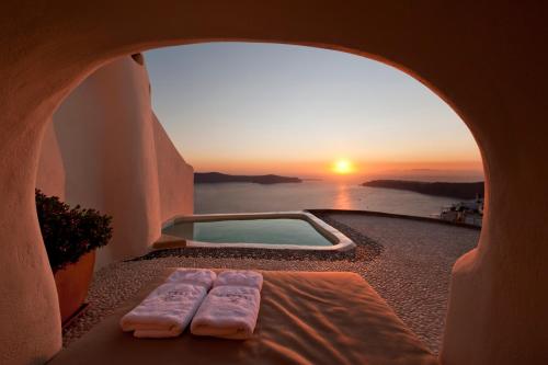 una finestra con vista sul tramonto e sulla piscina di Kapari Natural Resort a Imerovigli