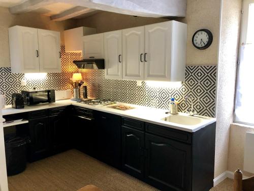 a kitchen with black cabinets and a clock on the wall at La Closerie - trois chambres in Vicq-sur-Gartempe