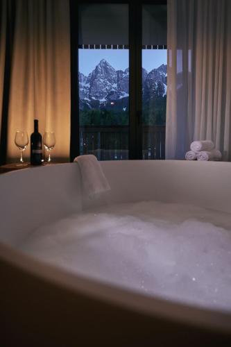 a bath tub with two wine glasses and a window at Triangel Boutique Hotel in Kranjska Gora