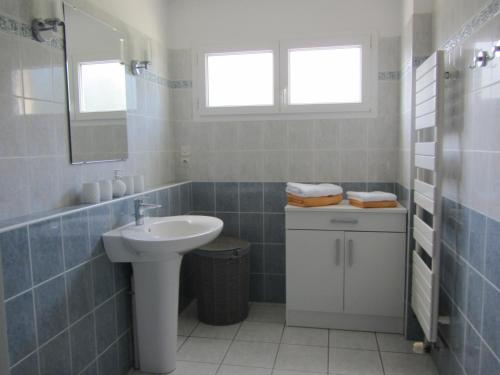 La salle de bains est pourvue de carrelage bleu, d'un lavabo et d'un miroir. dans l'établissement La Villa Marina, à Donville-les-Bains