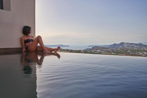 a woman sitting on the edge of a swimming pool at Apikia Santorini in Pirgos