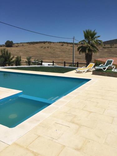 a swimming pool with two chairs and a palm tree at Turismo Rural Pão e Água in Mértola
