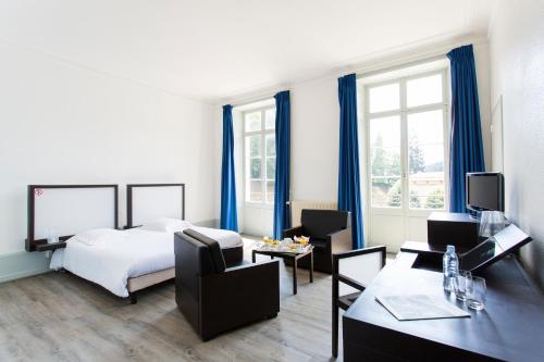プロンビエール・レ・バンにあるLe Grand Hotel de Plombières by Popinnsのベッド、テーブル、椅子が備わるホテルルームです。