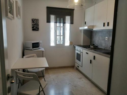 une cuisine avec des placards blancs, une table et une fenêtre dans l'établissement Room in Lovely cottage house Habitaciones en Chalet en Cadiz San Fernando, à San Fernando