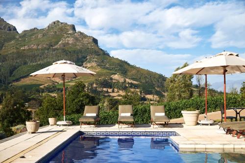 una piscina con sillas, sombrillas y una montaña en Alluvia Boutique Winery & Luxury Accommodation, en Stellenbosch