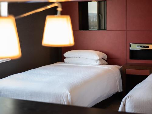 two beds in a hotel room with two lamps at Hotel Vista Sapporo Nakajima Koen in Sapporo