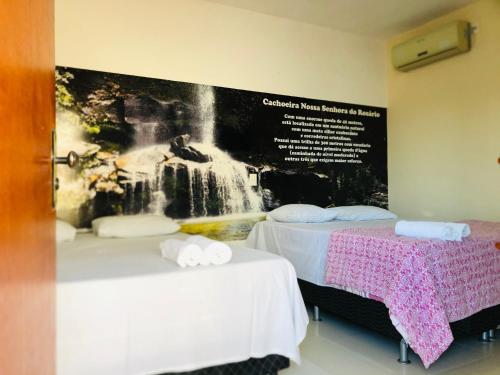 two beds in a room with a picture of a waterfall at Pousada Caminho das Cachoeiras Pirenopolis in Pirenópolis