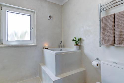 La salle de bains blanche est pourvue d'un lavabo et d'une fenêtre. dans l'établissement Casa Golden Bamboo, private patio & 100m from the river!, à Vila Nova de Milfontes