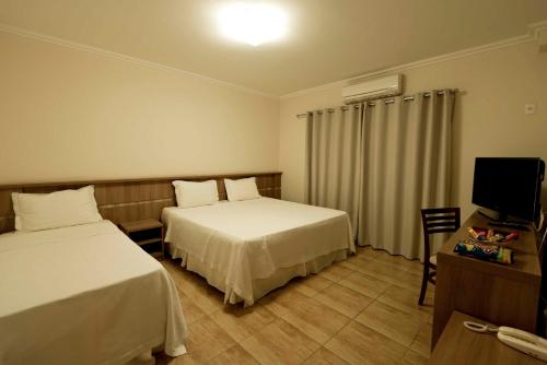 a hotel room with two beds and a television at Grand Enio Hotel e Cantina in Varginha