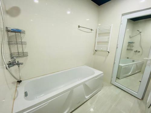 uma casa de banho branca com uma banheira e um espelho. em Pirosmani Apartment em Batumi
