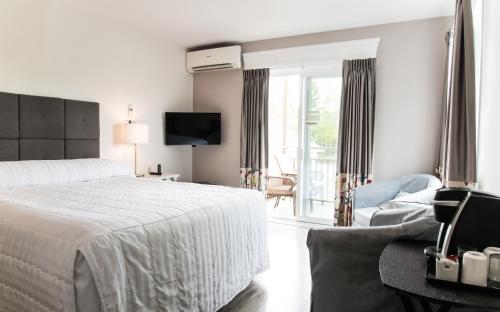 a white bedroom with a bed and a balcony at Hôtel Motel Le Beluga in Tadoussac