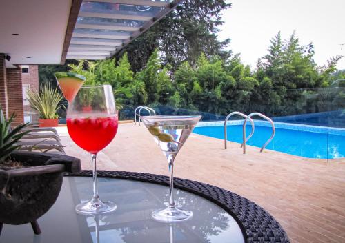 two glasses of wine sitting on a table near a pool at MG Hotels & Suites in Rionegro