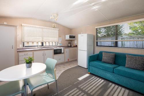 a living room with a blue couch and a table at Athenree Hot Springs & Holiday Park in Waihi Beach