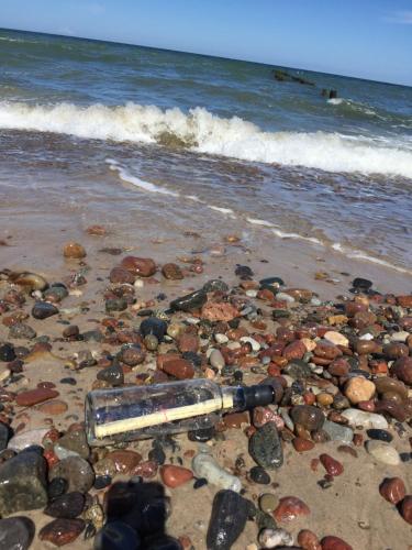 a bottle on a beach with rocks and water at Domki w Rusinowie blisko morza in Jarosławiec