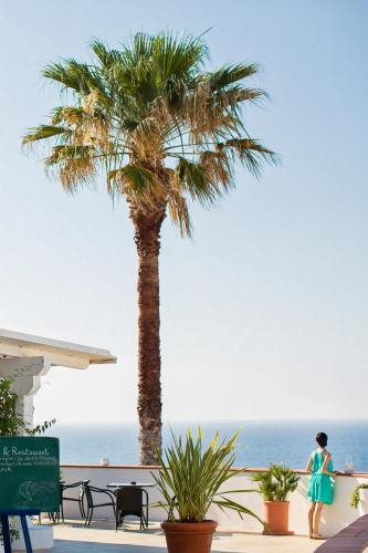 a woman walking past a palm tree next to the ocean at LH Pedraladda Resort in Castelsardo