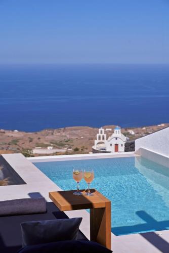 two wine glasses sitting on a table next to a swimming pool at Brilliance Suites in Imerovigli