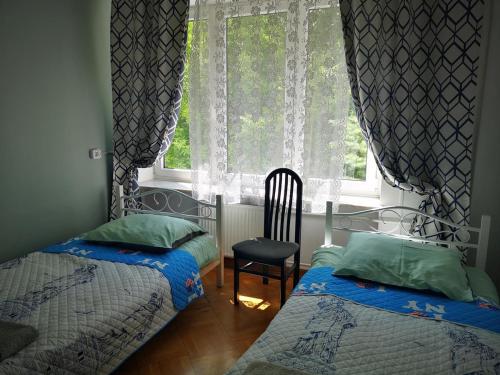 a bedroom with two beds and a window with a chair at Mira Rent House in Warsaw