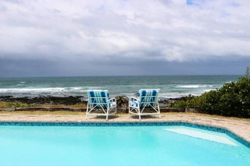 two chairs sitting next to a swimming pool with the ocean at Oceans End - a home on the beach in Kini Bay