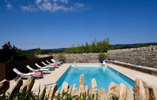 a swimming pool with lounge chairs and a stone wall at Gîte des Demoiselles en Luberon in Roussillon