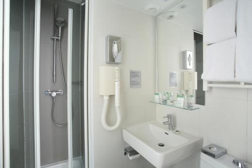 a white bathroom with a shower and a sink at Hotel Eiffel Capitol in Paris