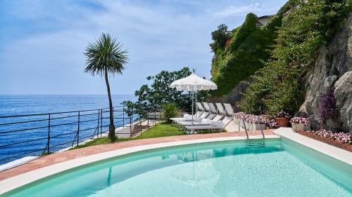 uma piscina com cadeiras e um guarda-sol junto ao oceano em Palazzo Avino em Ravello