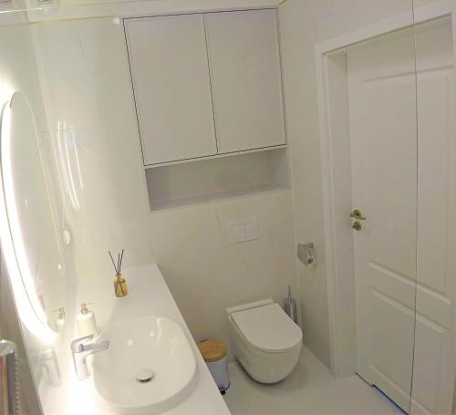 a white bathroom with a sink and a toilet at Niechorze Amber Sunset apartment in Niechorze