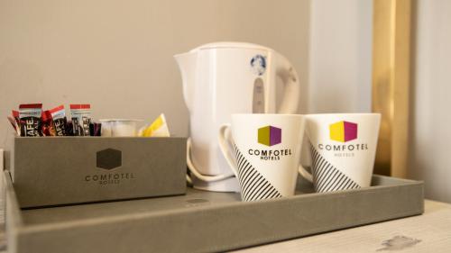 two coffee cups sitting on a shelf next to a coffee maker at Comfotel GRN in London