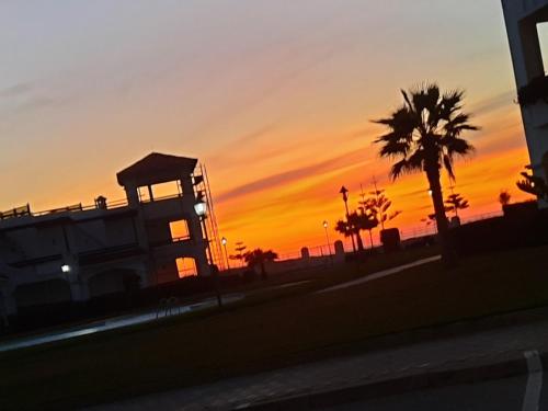 a sunset with a building and a palm tree at Appartement de vacances BERALMAR CHEZ HOUDA in Asilah