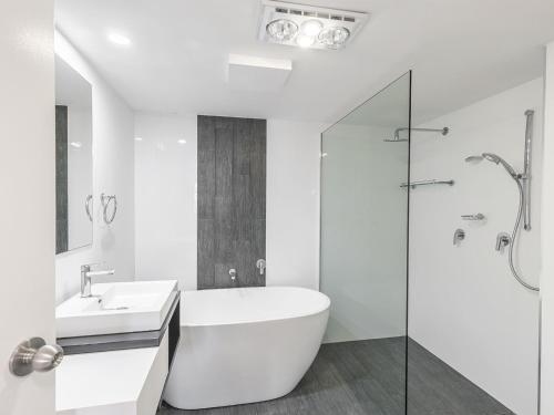 a white bathroom with a tub and a sink at Pelican Sands 2 fantastic waterfront unit with pool and air conditioning in Soldiers Point