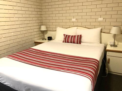 a bedroom with a white bed with a striped blanket at Golfview Motor Inn in Wagga Wagga
