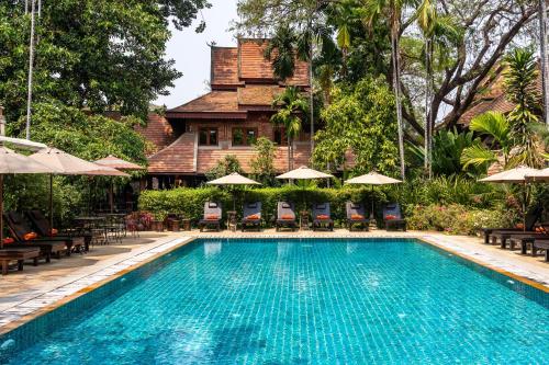 a swimming pool with chairs and umbrellas in front of a house at Yaang Come Village Hotel in Chiang Mai