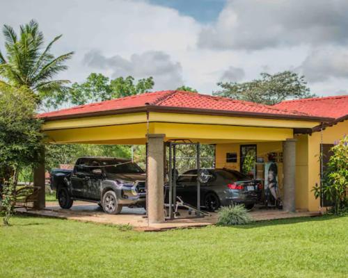 a small yellow house with a carport and cars parked at Linda casa de verano con amplias zonas verdes in San Isidro